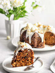 A piece of carrot cake decorated with icing, walnuts and Easter decor on a dessert plate on a light background