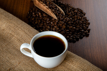 White cup of coffee with coffee beans on wooden background	
