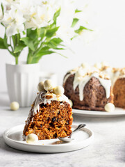 A piece of carrot cake decorated with icing, walnuts and Easter decor on a dessert plate on a light background
