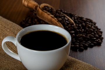 White cup of coffee with coffee beans on wooden background	