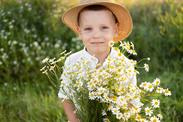 cute smiling child boy in straw hat holds bouquet of field chamomiles on sunset