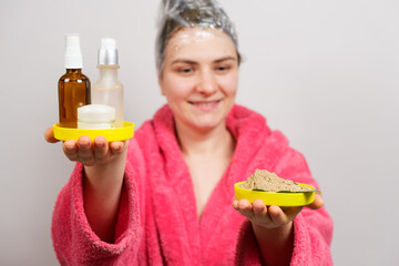 A woman with a film on her head makes a hair mask and holds natural and unnatural cosmetics in her...
