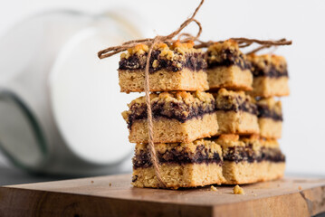 Pieces of the pie with currant jam are stacked and tied with twine. On a wooden board. On a gray table. Glass jar in the background.