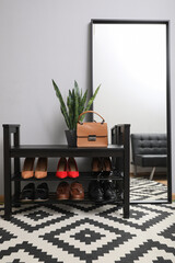 Shelving unit with stylish shoes and large mirror near grey wall in hallway