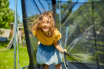 Portrait of young girl on her trampoline outdoors, in the backyard of the house on a sunny summer day