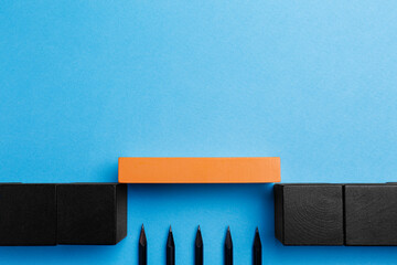 Bridge made of wooden blocks over trap with pencils as spikes on light blue background, flat lay
