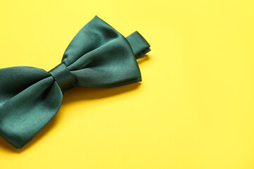 Stylish green satin bow tie on yellow background, closeup. Space for text