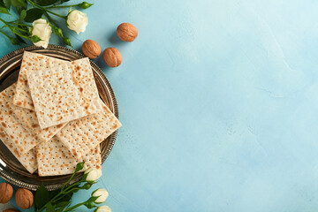 Passover celebration concept. Matzah, red kosher walnut and spring beautiful rose flowers. Traditional ritual Jewish bread on light turquoise or blue background. Passover food. Pesach Jewish holiday.