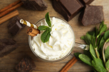 Glass cup of delicious hot chocolate with whipped cream and mint on wooden table, flat lay