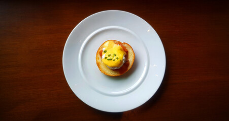 Flat ay of bread with poached egg, bacon and sweet sauce on top in dish. Top view of delicious meal of breakfast on white plate in American style. Close up food on table.