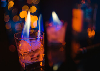 A bar counter with a bottle of alcoholic beverage and two square glasses with a burning blue flame...