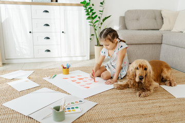 A girl draws hearts for his mother sitting on carpet floor in living room, cocker spaniel dog lying...