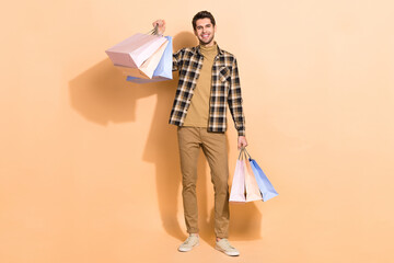 Full length body size view of attractive cheerful guy holding bags new things isolated over beige...