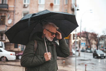Senior man with a headache with an umbrella in the rain. Stress and bad experiences.