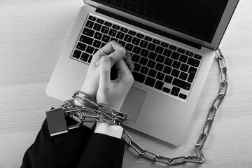Top view of woman with chained hands and laptop at wooden table, black and white effect. Internet...