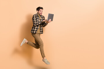 Full length body size view of attractive cheery skilled guy jumping using laptop copy space isolated on beige pastel color background