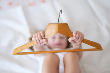 Child girl holding wooden hange closeup. Choosing clothes hanger