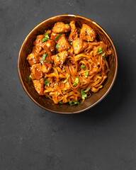 Udon noodles with chicken in teriyaki sauce in a brown bowl on a dark gray culinary background	
