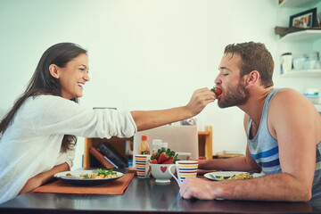 Berries for bae. Shot of a happy young woman feeding a strawberry to her boyfriend over the breakfast table.