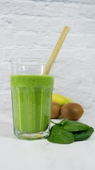 Fresh green spinach smoothie with kiwi and bananas in the background
