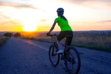 Fototapeta na wymiar Beautiful woman cyclist riding a bike on the road towards the sunset.