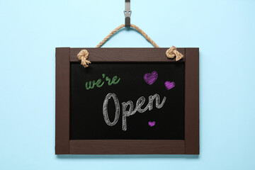 Small chalk board with phrase We're Open on light blue background