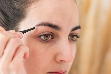 Close up portrait of young caucasian woman tweezing her eyebrows