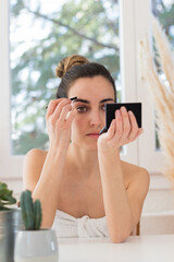 Woman from the shower twizzing her eyebrows in front of a mirror on a vanity