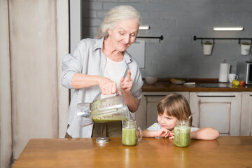 Healthy nutrition in the family, vegetarianism. Senior lifestyle. grandmother and granddaughter drink smoothie from greenery and superfoods in the kitchen at home