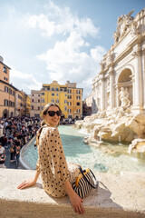 Woman visiting famous di Trevi fountain in Rome. Traveling Italy on a summer day concept. Portrait of caucasian woman in dress and shawl in hair - obrazy, fototapety, plakaty