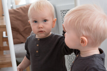 Fototapeta na wymiar Little blond boy looking at himself reflection in mirror at home