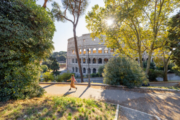Wide view on coliseum from park near by, small female figure running on path. Landscape of the most famous landmark in Rome - obrazy, fototapety, plakaty