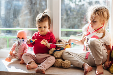 Teaching your child preventive measures against covid-19, viruses and flu. The girl in a protective mask is playing with her sister at the doctor. Care for loved ones. Basic hygiene rules. Pandemia.