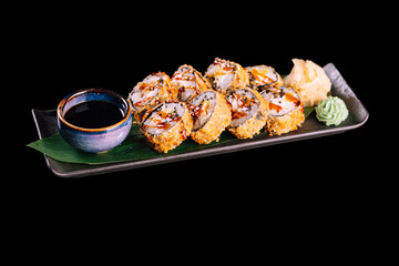 Breaded sushi set with smoked eel, sprinkled with sesame seeds. Served with ginger, wasabi and soy sauce on dark plate with green leaf, isolated on black background. Traditional Japanese seafood. 