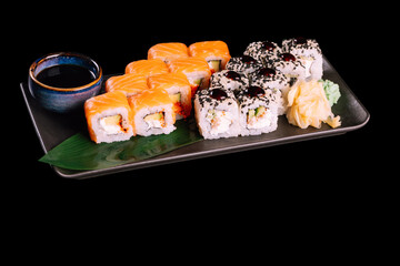 Served with ginger, wasabi and soy sauce on dark plate with green leaf, isolated on black background. Traditional Japanese seafood. 
