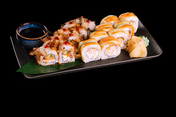 Varied sushi set. Served with ginger, wasabi and soy sauce on dark plate with green leaf, isolated on black background. Traditional Japanese seafood. 
