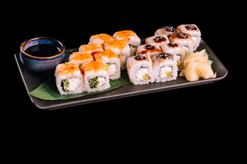 Varied sushi set. Served with ginger, wasabi and soy sauce on dark plate with green leaf, isolated on black background. Traditional Japanese seafood. 