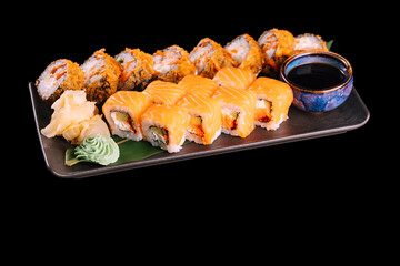 Varied sushi set. Served with ginger, wasabi and soy sauce on dark plate with green leaf, isolated on black background. Traditional Japanese seafood. 
