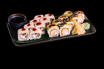 Varied sushi set. Served with ginger, wasabi and soy sauce on dark plate with green leaf, isolated on black background. Traditional Japanese seafood. 