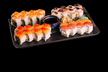 Varied sushi set. Served with ginger, wasabi and soy sauce on dark plate with green leaf, isolated on black background. Traditional Japanese seafood. 