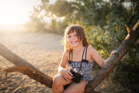 Cute european child girl in a bathing suit with binoculars on a tree. Summer holidays and adventures. Jungle games on the sea coast. - Powered by Adobe