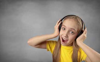 beautiful girl listening to music on headphones on grey background. Copy space for banner