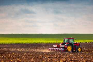 Farmer with tractor seeding crops at field