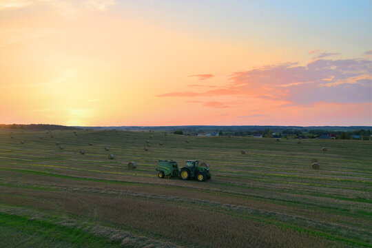 John Deere Tractor 6715R with John Deere V461R round baler making Hay Bales in an agricultural field. Farm Round Hay Bale Tractor Baler. Balers to roll. Russia, Smolensk, September 13, 2021.