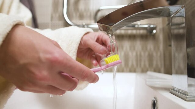 Close-up of unrecognizable caucasian young woman toothbrushing her kappa aligner under running water in bathroom sink. Care of dental accessories
