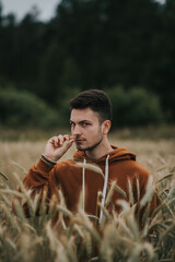 A young handsome guy with a small beard in a brown jacket in the middle of the field