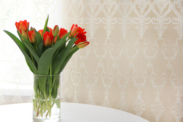 a bouquet of red tulips in a glass vase on a white table. Spring bouquet of flowers in a vase