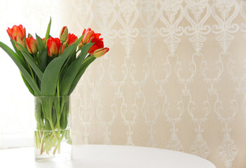 a bouquet of red tulips in a glass vase on a white table. Spring bouquet of flowers in a vase