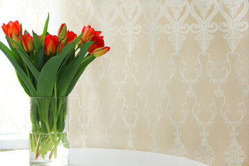 a bouquet of red tulips in a glass vase on a white table. Spring bouquet of flowers in a vase