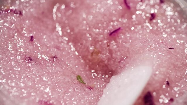 Close-up of the oily constitution of a pink body peeling based on sea salt and rose petals with bubbles slow stirring with a white plastic spatula. High quality 4k footage